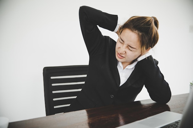 Young asian woman is sitting at work and has pain in her neck