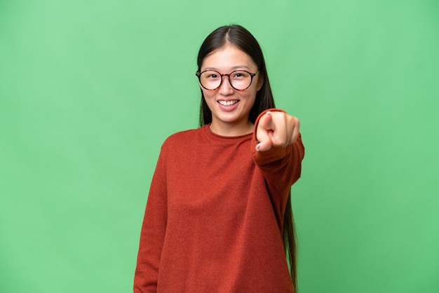 고립된 배경을 가진 젊은 아시아 여성이 무언가를 보기 위해 손을 멀리 내다보고 있습니다.