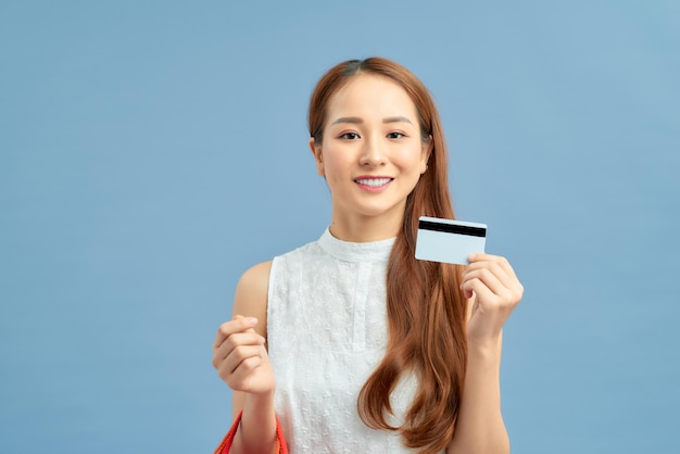 Young asian woman isolated on blue background holding shopping bags and a credit card