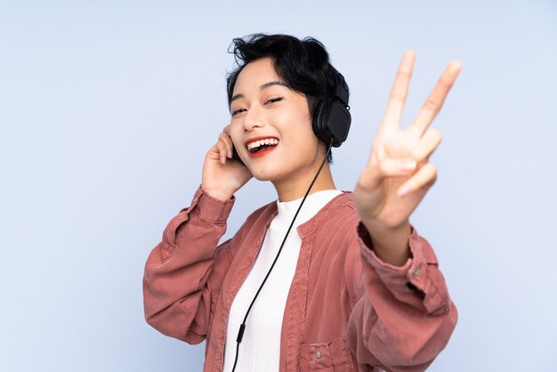 Young asian woman over isolated blue wall listening music and singing