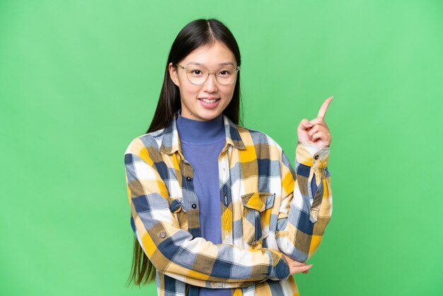 Young asian woman over isolated chroma key background happy and pointing up