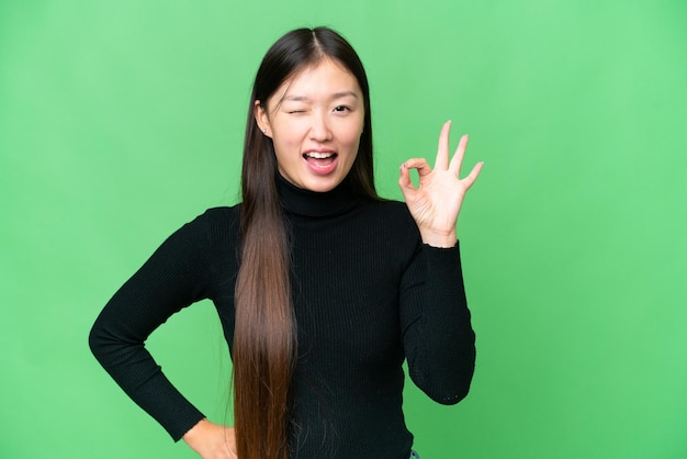 Young Asian woman over isolated chroma key background showing ok sign with fingers