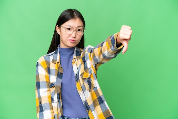 Young Asian woman over isolated chroma key background showing thumb down with negative expression