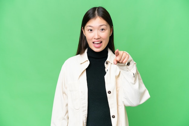 Young Asian woman over isolated chroma key background surprised and pointing front