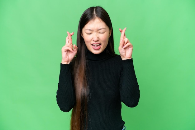 손가락이 교차하는 고립된 크로마 키 배경 위에 있는 젊은 아시아 여성