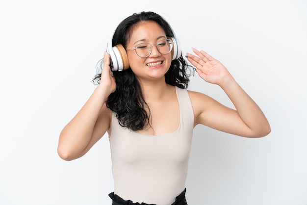 Молодая азиатская женщина изолирована на белом фоне, слушает музыку и поет