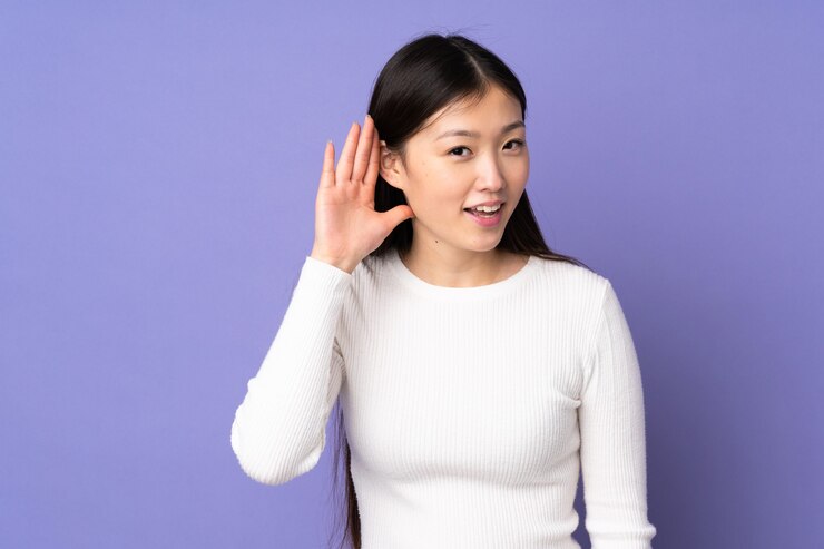 Photo 耳に手を置くことによって何かを聞いて紫色の背景で隔離の若いアジアの女性