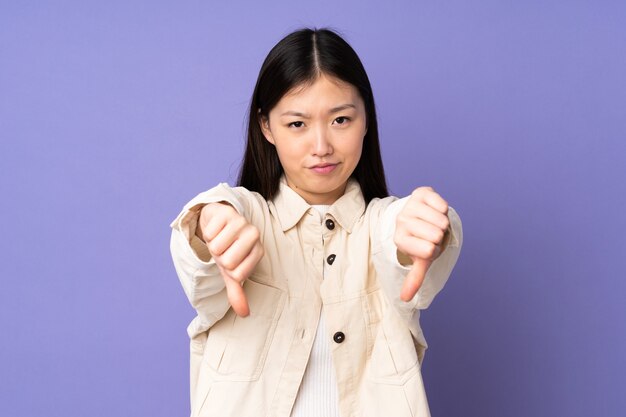 Young asian woman isolated on purple background showing thumb down with two hands