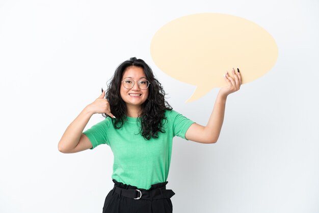 Young asian woman isolated on white background holding an empty speech bubble and doing phone gesture