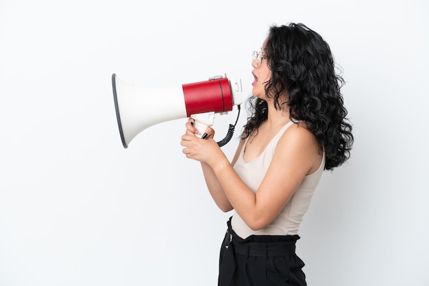 Young asian woman isolated on white background shouting through a megaphone to announce something in lateral position