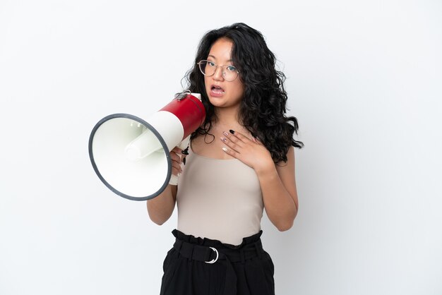 Young asian woman isolated on white background shouting through a megaphone with surprised expression