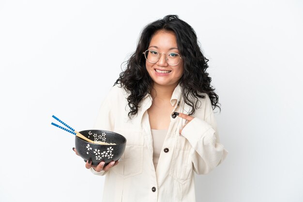 Young asian woman isolated on white background with surprise facial expression while holding a bowl of noodles with chopsticks