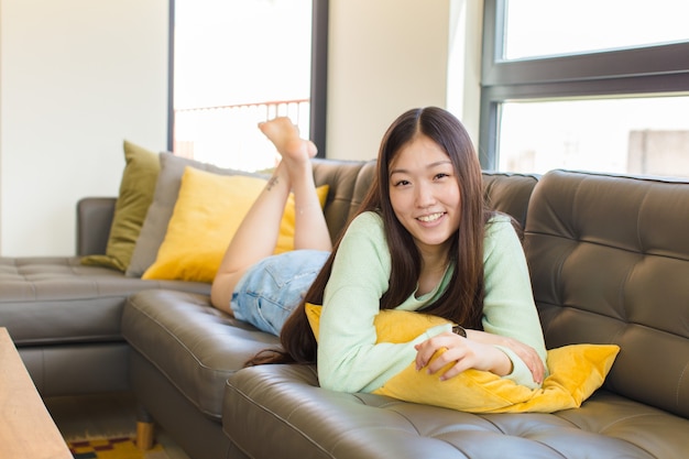 Young asian woman laughing shyly and cheerfully, with a friendly and positive but insecure attitude