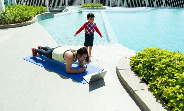   young Asian woman and little kid boy smiling while lying on yoga mat online training. Healthy Lifestyle and Sport Concepts.