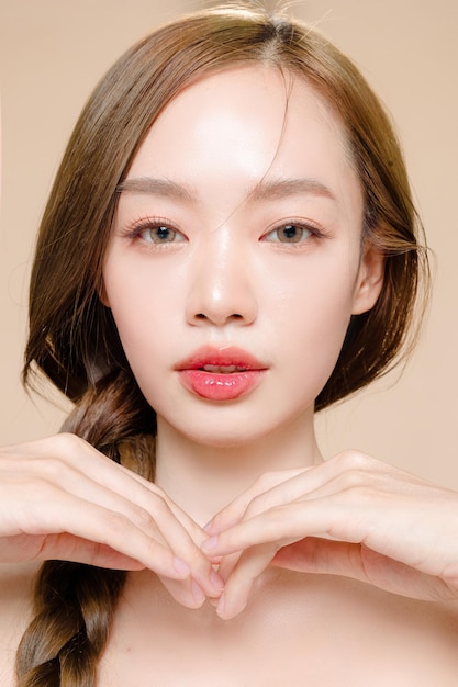 アジアの若い女性の長い髪の三つ編みの顔に自然な化粧と孤立したベージュの背景にきれいな新鮮な肌 スタジオでかわいい女性モデルの肖像 フェイシャルトリートメント 美容