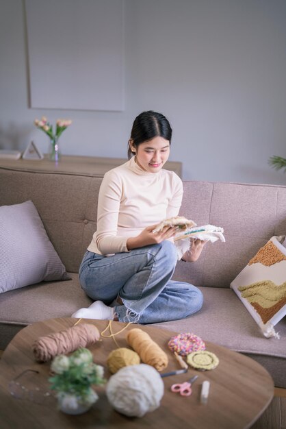 young asian woman looking on embroidery fabric frame with punch needle technique in hobby lifestyle