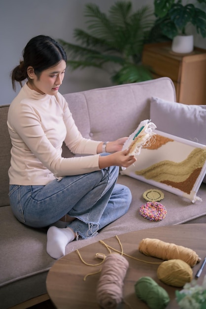 young asian woman looking on embroidery fabric frame with punch needle technique in hobby lifestyle