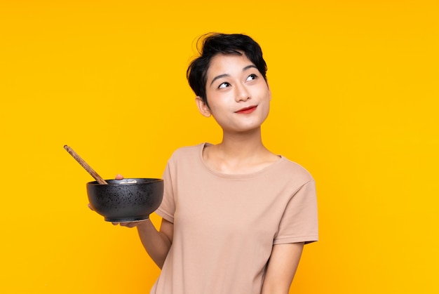 Young Asian woman looking up while smiling while holding a bowl of noodles with chopsticks