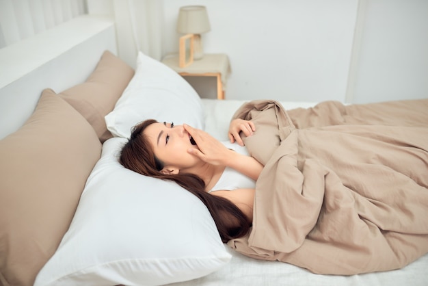 Young Asian woman lying on bed and yawning