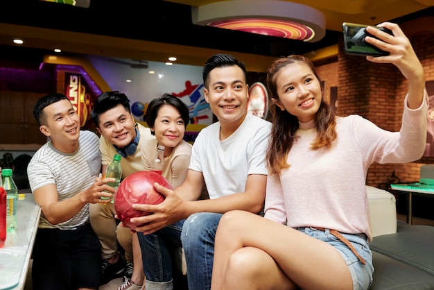 Giovane donna asiatica che fa selfie sul suo telefono cellulare insieme ai suoi amici mentre gioca a bowling