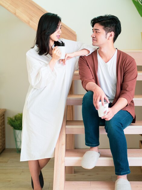 Young asian woman and man are enjoying spending time together at home with cup of coffee in hands.