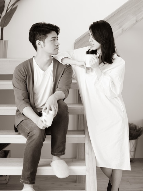 黒と白の手でコーヒーのカップを持つ自宅で若いアジアの女性と男性。