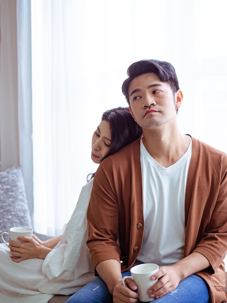 Young asian woman and man at home with cup of coffee in hands.