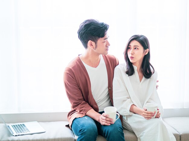 Young asian woman and man at home with cup of coffee in hands.