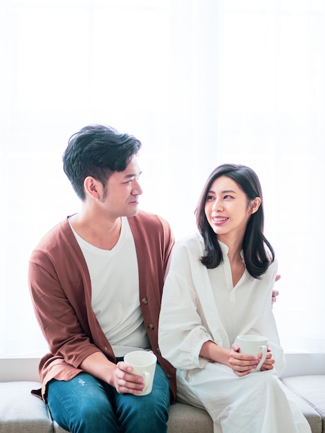 Young asian woman and man at home with cup of coffee in hands.