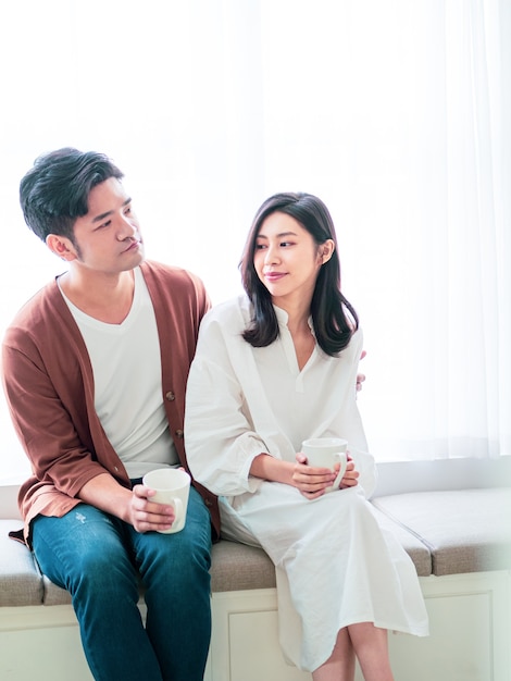 Young asian woman and man at home with cup of coffee in hands.