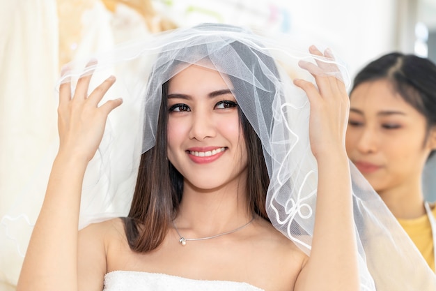 Молодая азиатская женщина измеряя на платье свадьбы в магазине портноем.