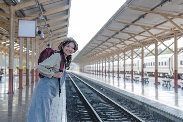 현대 기차역에서 젊은 아시아 여성 여성 배 여객이 기차에서 기차를 기다리고 있습니다.