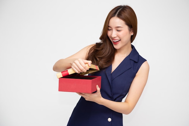 Giovane donna asiatica che apre scatola regalo d'oro con fiocco in nastro isolato su sfondo bianco