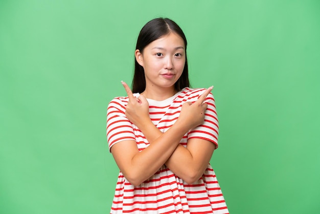 사진 고립된 배경을 가진 젊은 아시아 여성이 옆구리를 가리키며 제품을 제시합니다.