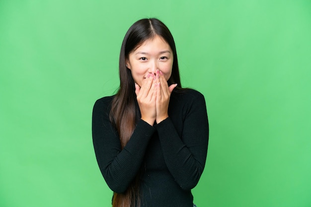 사진 고립된 크로마 키 배경을 가진 젊은 아시아 여성은 행복하고 손으로 입을 가리고 웃고 있습니다.