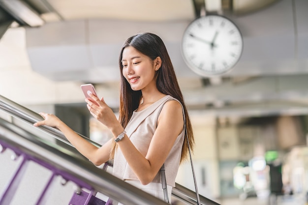 スマート携帯電話を使用して地下鉄の駅の階段を上る若いアジアの女性の乗客