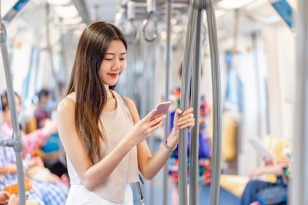 Passeggero giovane donna asiatica che utilizza il social network tramite telefono cellulare intelligente nel treno della metropolitana quando si viaggia in una grande città, giapponese, cinese, stile di vita coreano e vita quotidiana, pendolari e concetto di trasporto