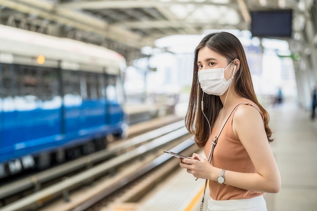 Young Asian woman passenger wearing surgical mask and listening music via smart mobile phone