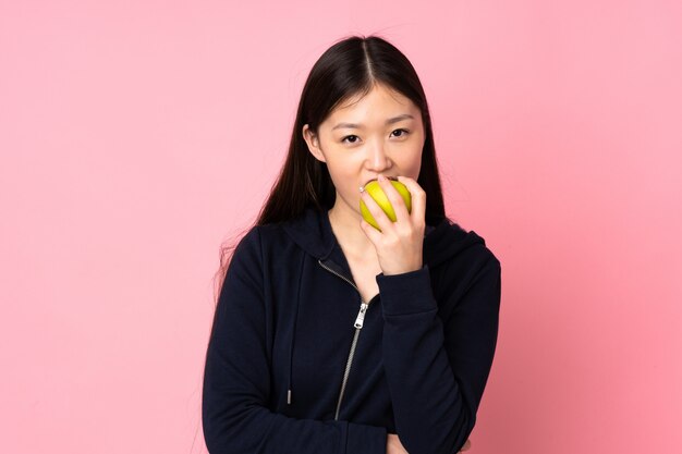 Young asian woman on pink wall eating an apple