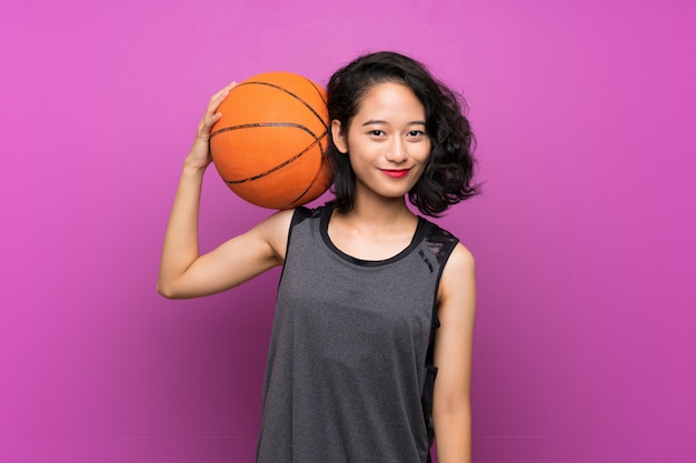 Young Asian woman playing basketball over purple wall