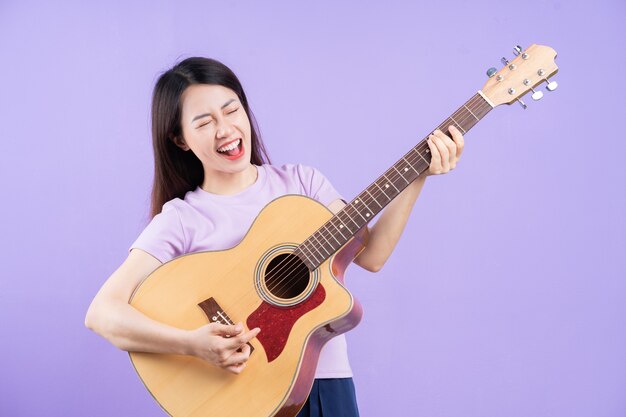 Young Asian woman playing guitar on purple background