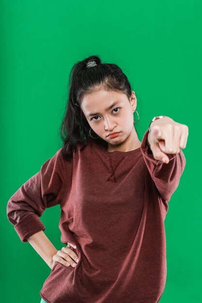 Young Asian woman pointing at the camera while expression pissed off the face in green background