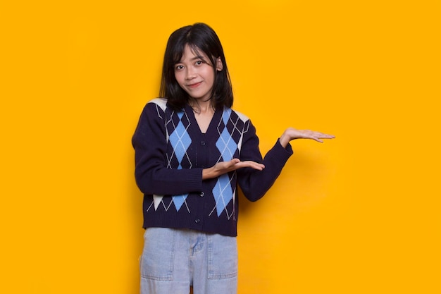 young asian woman pointing with fingers to different directions isolated on yellow background