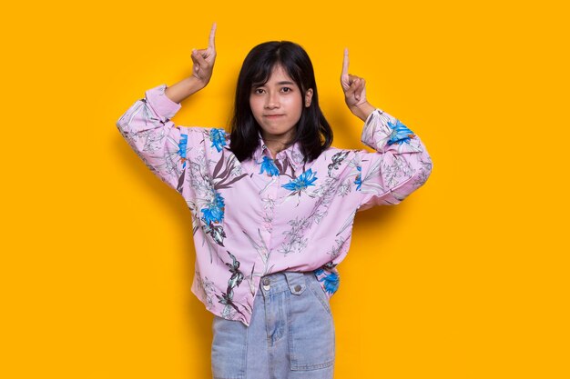 Young asian woman pointing with fingers to different directions isolated on yellow background