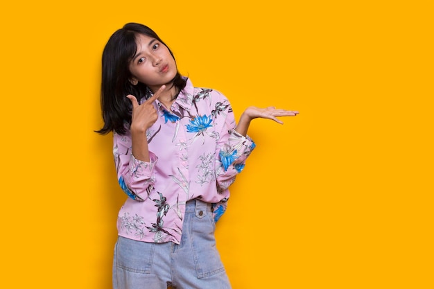 молодая азиатка, указывающая пальцами в разные стороны на желтом фоне