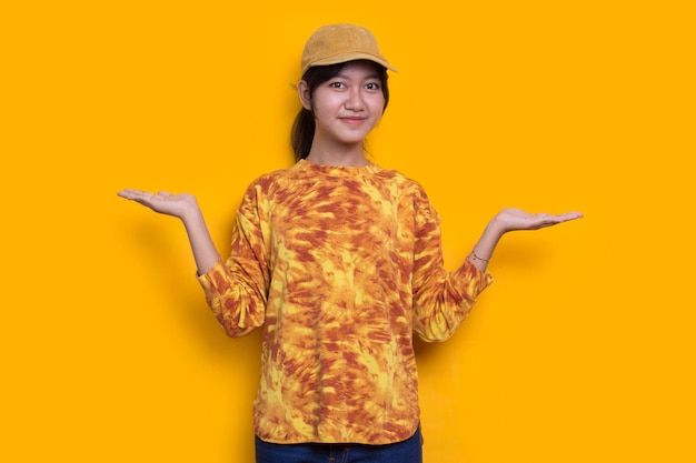 young asian woman pointing with fingers to different directions isolated on yellow background