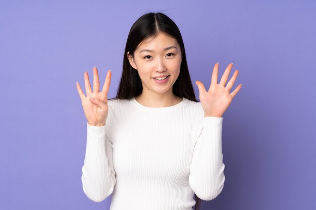 指で9を数える紫色の壁に若いアジア女性