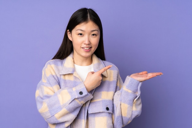 Young asian woman on purple wall holding blank space on the palm