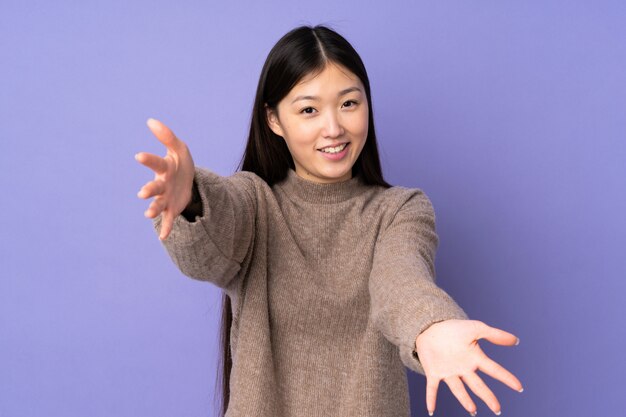 Young asian woman on purple wall presenting and inviting to come with hand