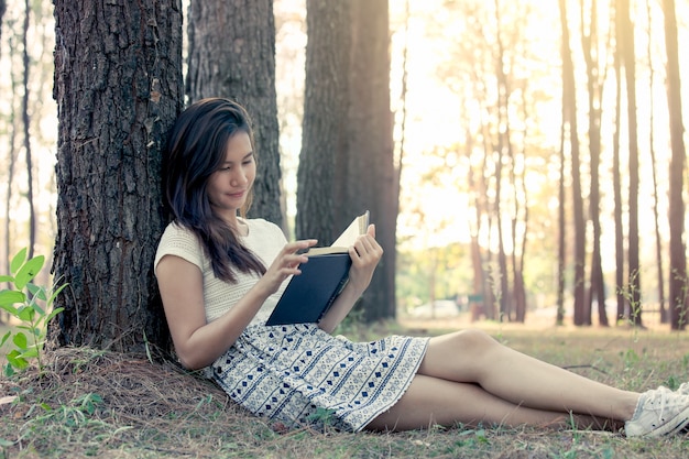 Молодая женщина Азии, чтение книги в парке в цветочном тоне